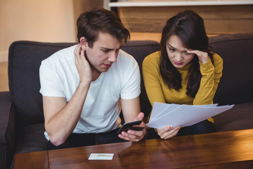 Confused couple reviewing insurance documents and bills, discussing financial options at home.