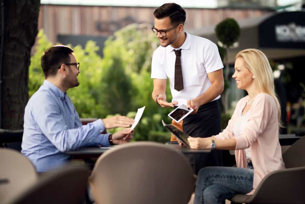Business meeting outdoors with three people discussing documents and tablet.