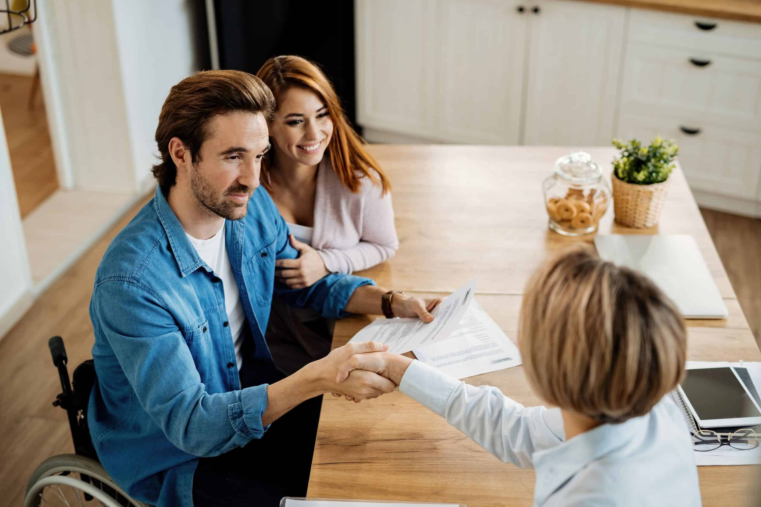 Friendly insurance advisor shaking hands with a client in a wheelchair, discussing coverage options.